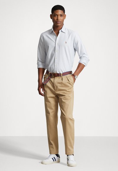 Lyseblå stripped skjorte med knapper, khaki bukser og et multicolor bælte. Hvide sneakers med marineblå striber. Simpelt design og afslappet pasform.