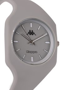 Reloj de silicona gris con una caja redondeada, esfera minimalista, marcadores de hora plateados y logo de Kappa en negro en la carátula.