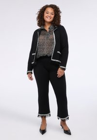 Černý blazer s krajkami ve stříbrné barvě, přes černobíle vzorovanou blůzu a černé rozšířené kalhoty s třásněmi na okrajích. Černé podpatky.