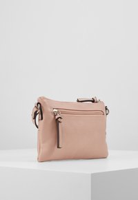 Růžová syntetická kožená crossbody taška s texturovaným povrchem, obsahující přední kapsu na zip a nastavitelný popruh s kovovými akcenty.