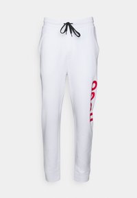 Hvide sweatpants med sorte snore, der har et stort rødt grafikdesign på venstre ben. Lavet af blødt stof med tætsiddende ankeldesign.
