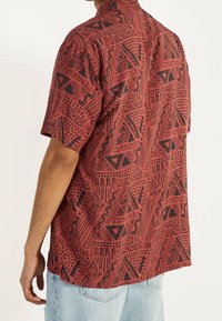 Camisa de manga corta en rojo con patrones tribales negros, con cuello tipo polo, tejido ligero y un ajuste relajado.
