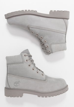 Paire de bottines lacées gris clair avec semelles épaisses en caoutchouc et col rembourré, placées sur fond blanc, montrant les vues latérale et de la semelle.
