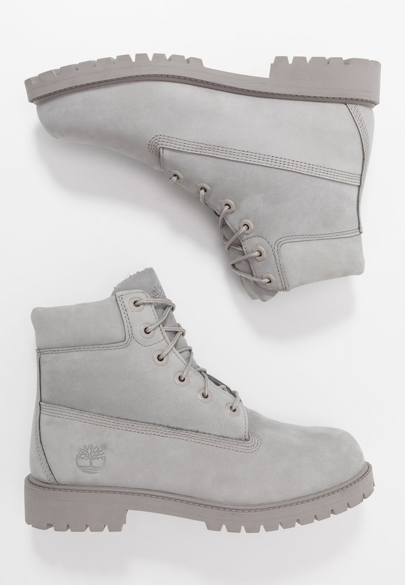 Paire de bottines lacées gris clair avec semelles épaisses en caoutchouc et col rembourré, placées sur fond blanc, montrant les vues latérale et de la semelle.