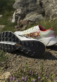 Weiße und orangefarbene Trailrunning-Schuhe auf felsigem Boden mit aggressiven schwarzen Sohlen mit Continental Markenprofil.