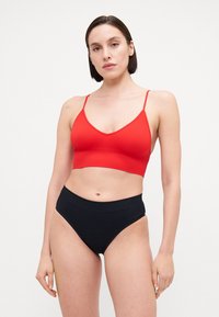 Bralette rouge côtelé avec bretelles ajustables, associé à des culottes noires taille haute. Tissu lisse avec un design ajusté et une texture légèrement extensible.