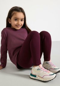 Langærmet maroon top parret med matchende leggings, suppleret af multicolore sneakers med en tekstureret sål og snørebåndsdetaljer.