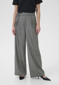 Pantalones de pierna ancha en rayas grises y blancas con cintura anudada y pliegues, confeccionados en una tela texturizada, combinados con tacones negros.