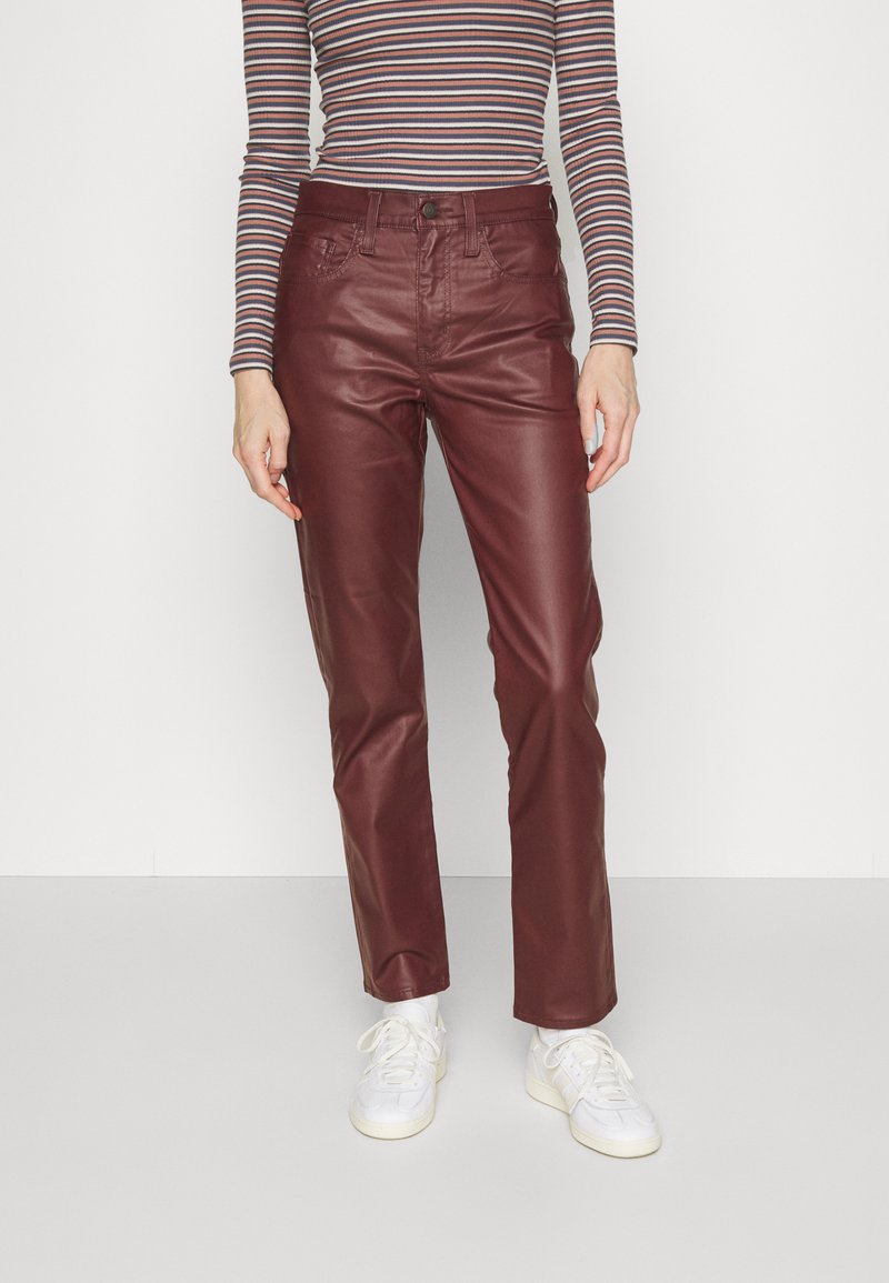 Bordeaux-farbene Kunstlederhosen mit slim fit, fünf Taschen und Knopfverschluss, kombiniert mit weißen Sneakern. Gestreiftes Hemd sichtbar.