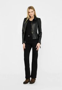 Mustast nahast jakk, millel on figuuri järgnev lõige, lukk ja kraega kaelus. Ühitatud musta toppi ja lehvikukujuliste mustade pükstega. Pruunid saapad.