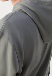 Felpa grigia con cappuccio caratterizzata da una texture morbida e liscia, con dettagli di cucitura visibili e una vestibilità casual evidenziata dal collo rilassato.