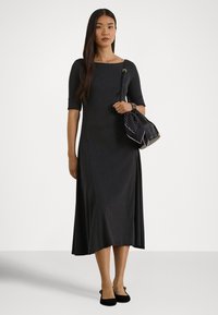 Melna midi kleita ar īsām piedurknēm un kvadrātveida izgriezumu, ar gludu faktūru. Kombinēta ar melnu somiņu un melnām baleta kurpēm.