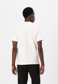 Polo shirt bianco in cotone con maniche corte, colletto classico e orlo dritto. Design minimalista senza modelli o accenti visibili.