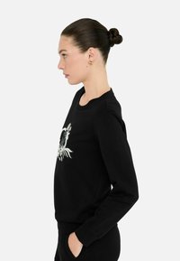 Zwarte sweatshirt met een ronde hals en lange mouwen, versierd met een centraal grafisch ontwerp van bloemmotieven en een cirkelvormig motief.