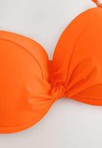 Haut de bikini orange vif avec bonnets rembourrés et un détail de nœud central, présenté sur un fond clair uni.