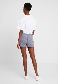 Grey cotton shorts with elastic waist and casual fit, paired with a plain white t-shirt and white sneakers, viewed from the back.