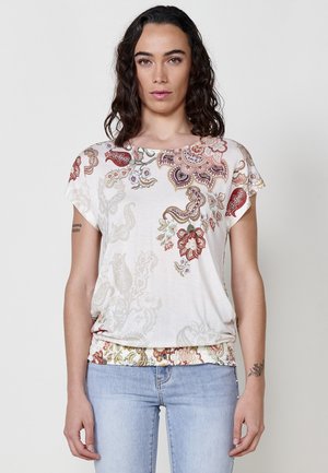 Chemise blanche à manches courtes avec des motifs floraux et paisley colorés, tissu doux, coupe décontractée, ourlet froncé et légères variations de texture.