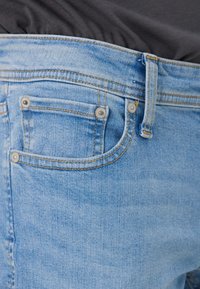 Hellblaue Denim-Jeans mit einer ausgewaschenen Optik, ausgestattet mit einer kleinen Fronttasche, silbernen Beschlägen und sichtbaren Nähdetails.