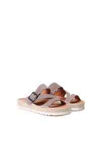 Brūnas suede slaidu sandales ar krusteniskām siksnām un sprāvēm, uz teksturētas espadrilles stila zoles ar baltu gumijas pamatni.