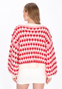 Hæklet sweater med en diamantmønster i nuancer af rød og pink. Løs pasform med ballonærmer, ribbet kant og blød tekstur.