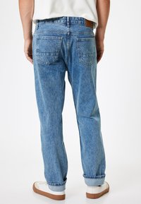 Jeans in denim azzurro chiaro con una vestibilità rilassata, dotati di due tasche posteriori e orli arrotolati all'estremità. Fettuccia in pelle marrone con il marchio sulla cintura.