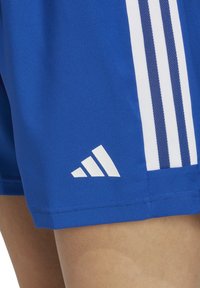 Blaue Sportshorts mit weißen Drei-Streifen-Akzenten und einem kleinen weißen Adidas-Logo, das nahe dem Saum platziert ist. Glatte Textur und sportliche Passform.