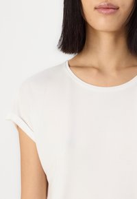 Weißes, kurzärmliges Oberteil mit rundem Ausschnitt, aus glattem Stoff gefertigt, mit umgeschlagenen Ärmelbündchen und einem minimalistischen Design.