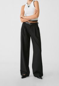 Pantalons larges noirs avec des plis, dotés d'une ceinture noire. Associés à un haut sans manches blanc. Texture de tissu lisse.