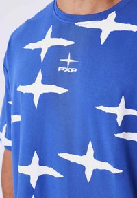 Camiseta de algodón azul con grandes motivos de estrellas blancas. Cuello redondo y pequeño logo "PXP" en el pecho. Textura suave. Manga corta.