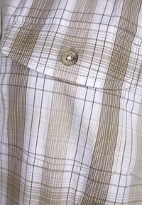 Camicia a quadri in beige e bianco con strisce verticali e orizzontali. Presenta una chiusura a bottoni e un piccolo dettaglio con il logo.
