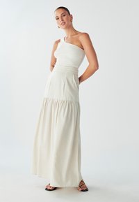 Kremowy, prążkowany top na jedno ramię zestawiony z przewiewną, warstwową spódnicą maxi. Stylizacja ma smukłą sylwetkę i teksturowane wykończenie. Czarne sandały.