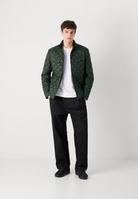 Veste verte matelassée avec fermeture éclair à l'avant, col montant et deux poches poitrine. Portez-la par-dessus une chemise blanche avec un pantalon noir ample et des chaussures noires.