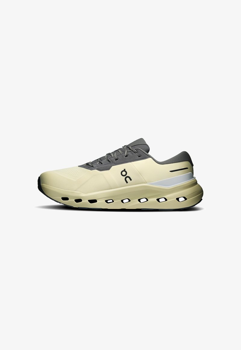 Chaussure de course beige clair et grise avec logo noir, semelle perforée et design à lacets vue de côté sur fond blanc.
