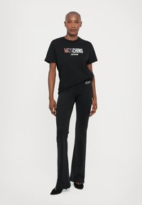 Čierne tričko s viacfarebným logom "Moschino Jeans", spárované s čiernymi rozšírenými nohavicami. Obe vyrobené z ľahkej tkaniny, s minimalisticými akcentmi.