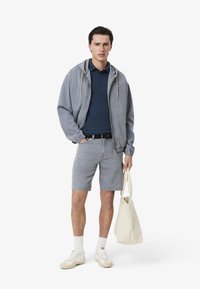 Jeans hoodie och ljusblå polo över jeansshorts, kombinerat med vita sneakers och en beige tygkasse. Enkel, avslappnad design.