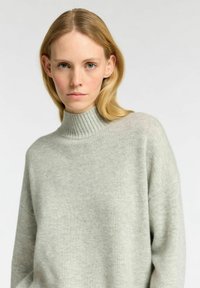 Světle šedý, oversized pletený svetr s kostkovaným vysokým límcem a spuštěnými rameny. Měkká textura, minimalistic design, bezešvá konstrukce.