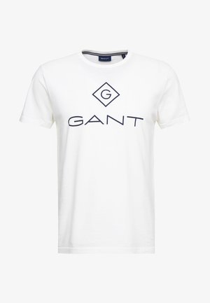 T-shirt en coton blanc avec un logo bleu marine en forme de diamant et le mot "GANT" imprimé en gros caractères sur la poitrine. Manches courtes, col rond.