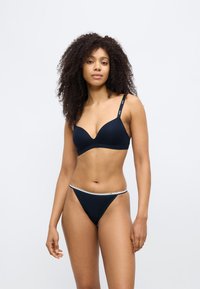 Laivastonsininen rintaliivi syvällä pääntiellä ja säädettävillä olkaimilla, yhdistettynä samanlaiseen matalavyötäröiseen tanga-alushousuihin, joissa on kontrastivärinen vyötärönauha.