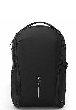 Mochila negra hecha de tejido texturizado, con un diseño delgado, bolsillo frontal con cremallera, asa en la parte superior y detalle del logo en el lateral.