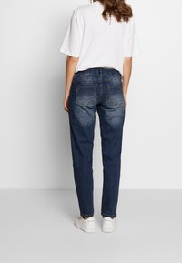 Mörkblå denimjeans med avslappnad passform, med bakfickor och lätt blekning. Kombinerat med en vit t-shirt med kort ärm och sneakers.