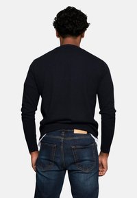 Granatowy sweter typu knit z długimi rękawami, okrągłym dekoltem i gładką fakturą, noszony z ciemnymi dżinsami z tylnymi kieszeniami.