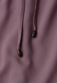 Gros plan d’un tissu mauve avec deux cordons assortis, chacun se terminant par une perle en bois foncé.