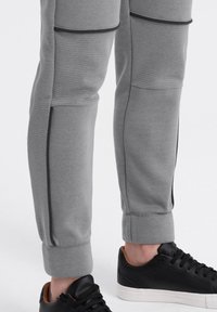 Graue Sweatpants mit strukturierten Ripp-Panels, schlankem Schnitt und schmal zulaufenden Bündchen, kombiniert mit einem schwarzen Sneaker, der ein glattes Finish aufweist.