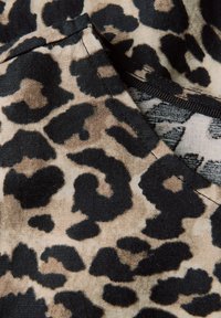 Látka s leopardím vzorem v béžové a černé barvě s hladkým povrchem, obsahující nepravidelné zvířecí skvrny a prošitý okraj.