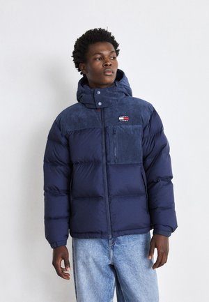  giubbotto imbottito blu navy con colletto in velluto a coste e tasca sul petto. Presenta una cerniera e bottoni, abbinato a jeans in denim azzurro.