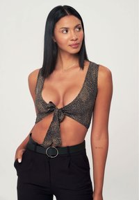 Crop top leopard print marrone e nero con nodo frontale, spalline larghe e lati tagliati, abbinato a pantaloni neri a vita alta e una cintura.