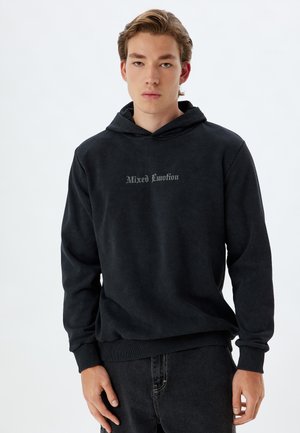Sudadera negra con una textura suave y un gráfico en la parte delantera que dice "Función Mixta" en gris claro. Cuenta con un bolsillo canguro y puños acanalados.