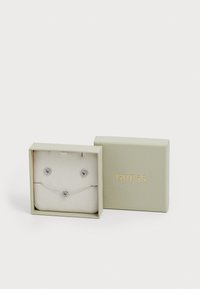 Zilveren hartvormige oorbellen en armband set gepresenteerd in een lichtgroene doos met een gestructureerd oppervlak en gouden "GUESS" branding.