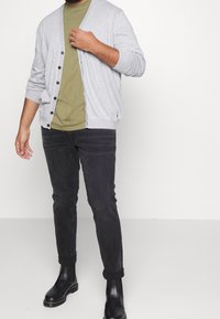 Šedý pletený kardigan s knoflíky, olivově zelené tričko pod ním, černé džíny a černé kotníkové boty. Jednoduchý a neformální outfit.