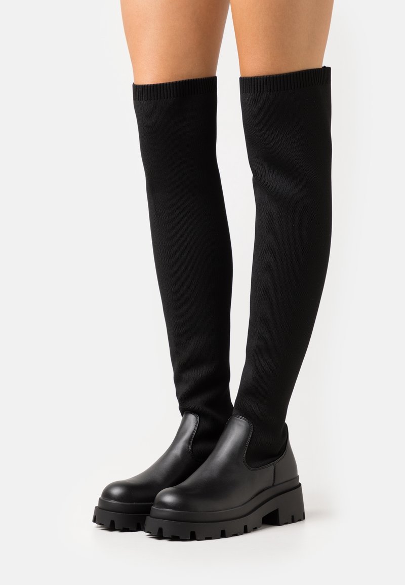 Mustat polven yli ulottuvat saappaat, joissa on sulavalinjainen nahkapohja ja pehmeä neulottu varsi. Varustettu paksulla kumipohjalla, jossa on kuvioitu pito.